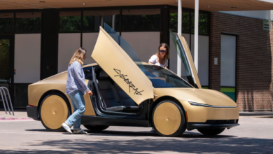 Two women stand beside a gold Tesla Cybercab with its futuristic butterfly doors open wide.