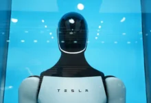 Close-up front view of the Tesla Optimus humanoid robot head and torso against a bright blue background