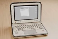A miniature retro laptop dubbed TinyMac 84 sitting open on a light wooden surface.