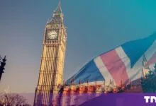 Big Ben tower in London overlaid with a large British Union Jack flag under a blue sky.