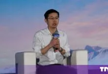 Wang Xingxing sitting in a white armchair holding a microphone during a conference panel.