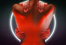Close-up of a bare back with red light casting a silhouette against a glowing white circle.