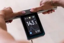 Close-up of hands holding a smart scale handle displaying a weight of 143.1 pounds.
