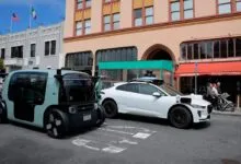 Autonomous Zoox and Waymo self-driving vehicles parked on a city street.